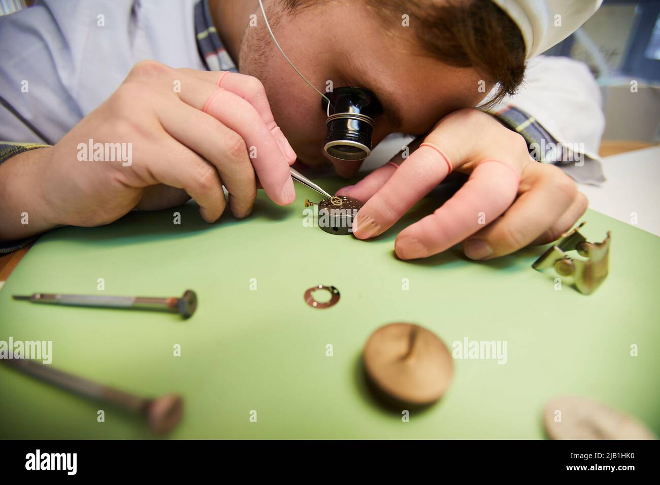 Close-up of concentrated engineer of wristwatch factory wearing monocular magnifying glass using tweezers while assembling watch mechanism Stock Photo