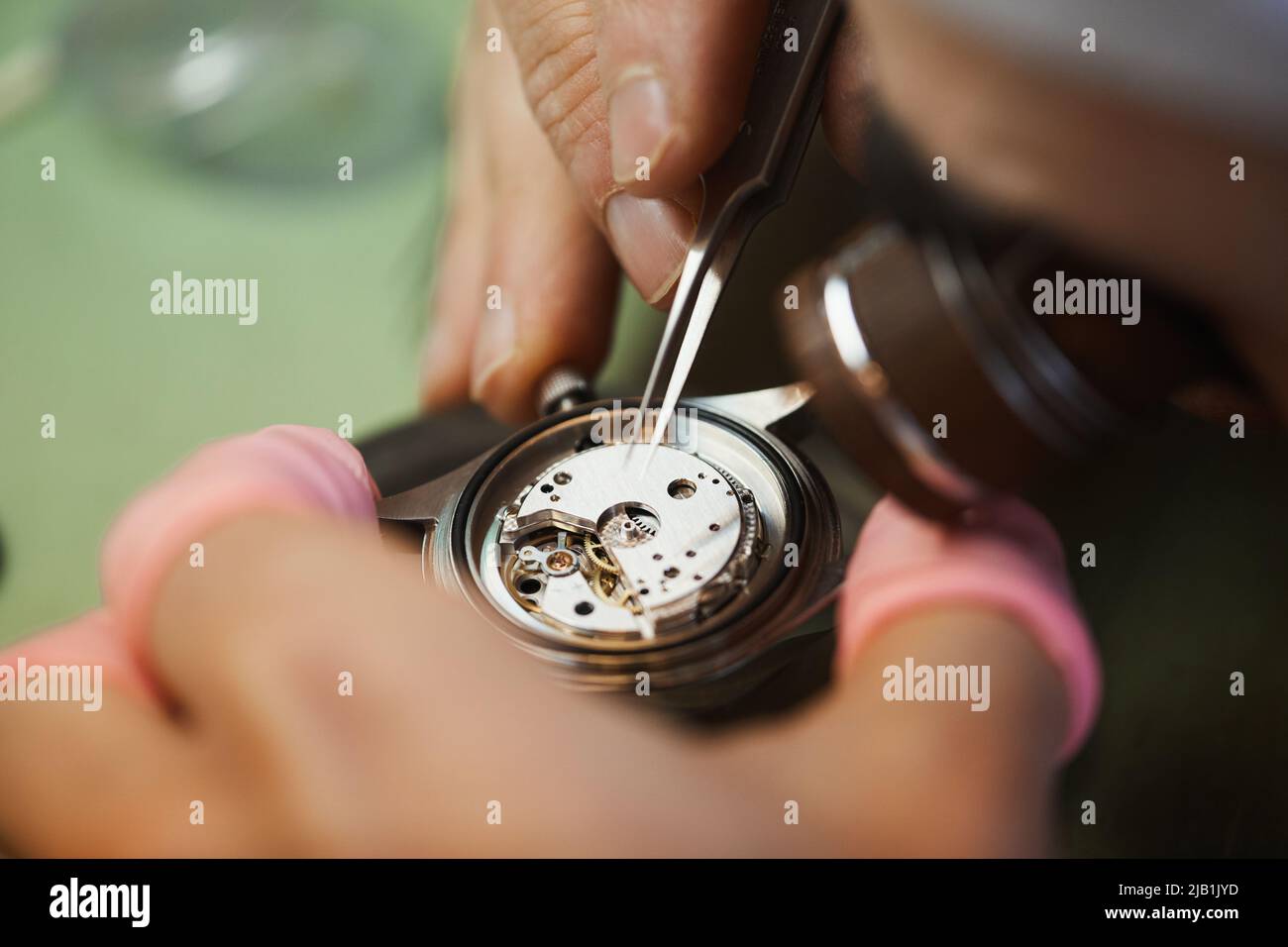 Macro of busy unrecognizable assembling engineer performing tedious work with watch cogs while examining mechanism Stock Photo