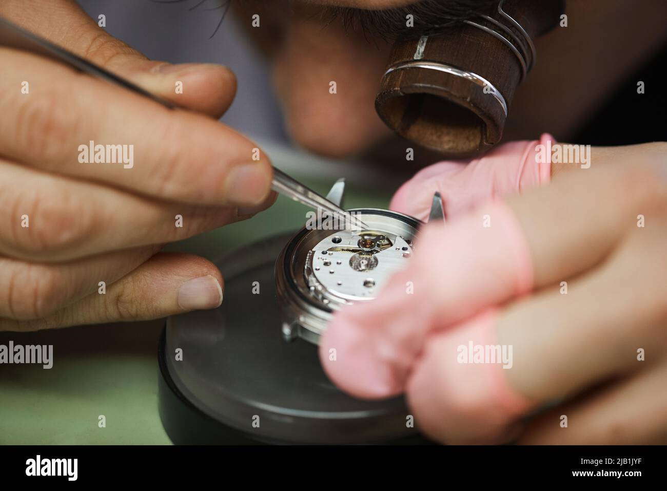 Close-up of concentrated engineer in monocular loupe on eye using tweezer while adjusting cog of wristwatch Stock Photo