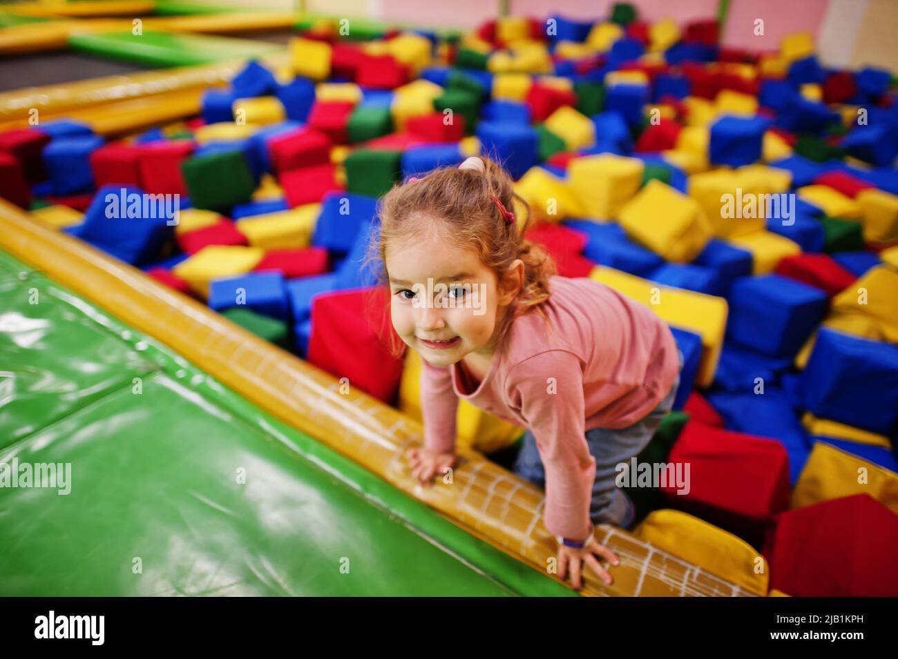 Cute baby girl lying on pool with colored foam cubes in indoor play