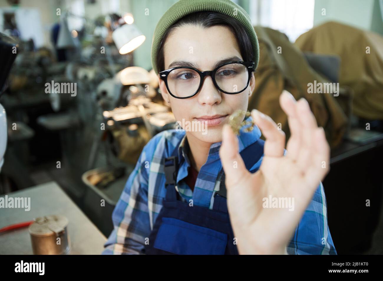 Serious thoughtful smart lady engineer in glasses examining small detail while working at watch production plant Stock Photo