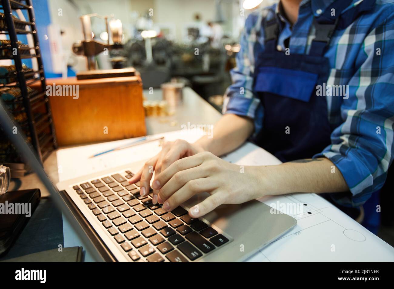 Close-up of unrecognizable woman engineer standing at desk with project plan and using laptop while searching for information on Internet Stock Photo
