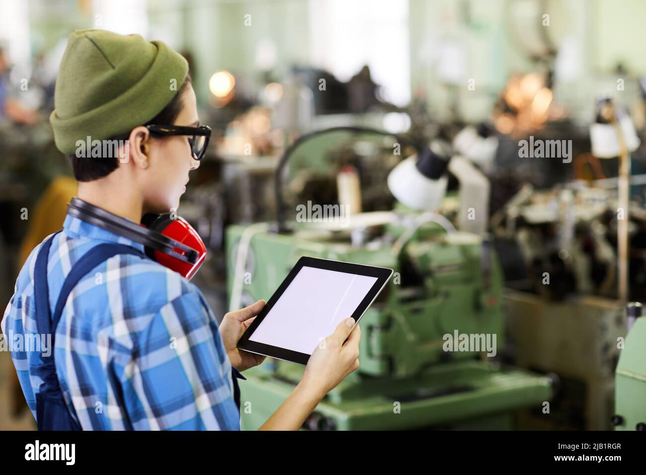 Serious quality control engineer in glasses using tablet for expertise while examining technical equipment at factory Stock Photo