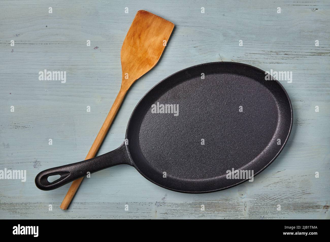 https://c8.alamy.com/comp/2JB1TMA/oval-cast-iron-frying-pan-with-a-wooden-spatula-on-a-blue-wooden-table-template-for-laying-out-dishes-2JB1TMA.jpg