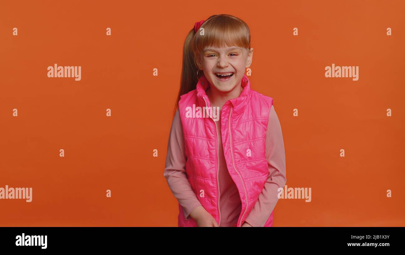 Joyful girl laughing out loud after hearing ridiculous anecdote, funny joke, feeling carefree amused, positive people lifestyle. Young little child kid isolated alone on orange studio wall background Stock Photo