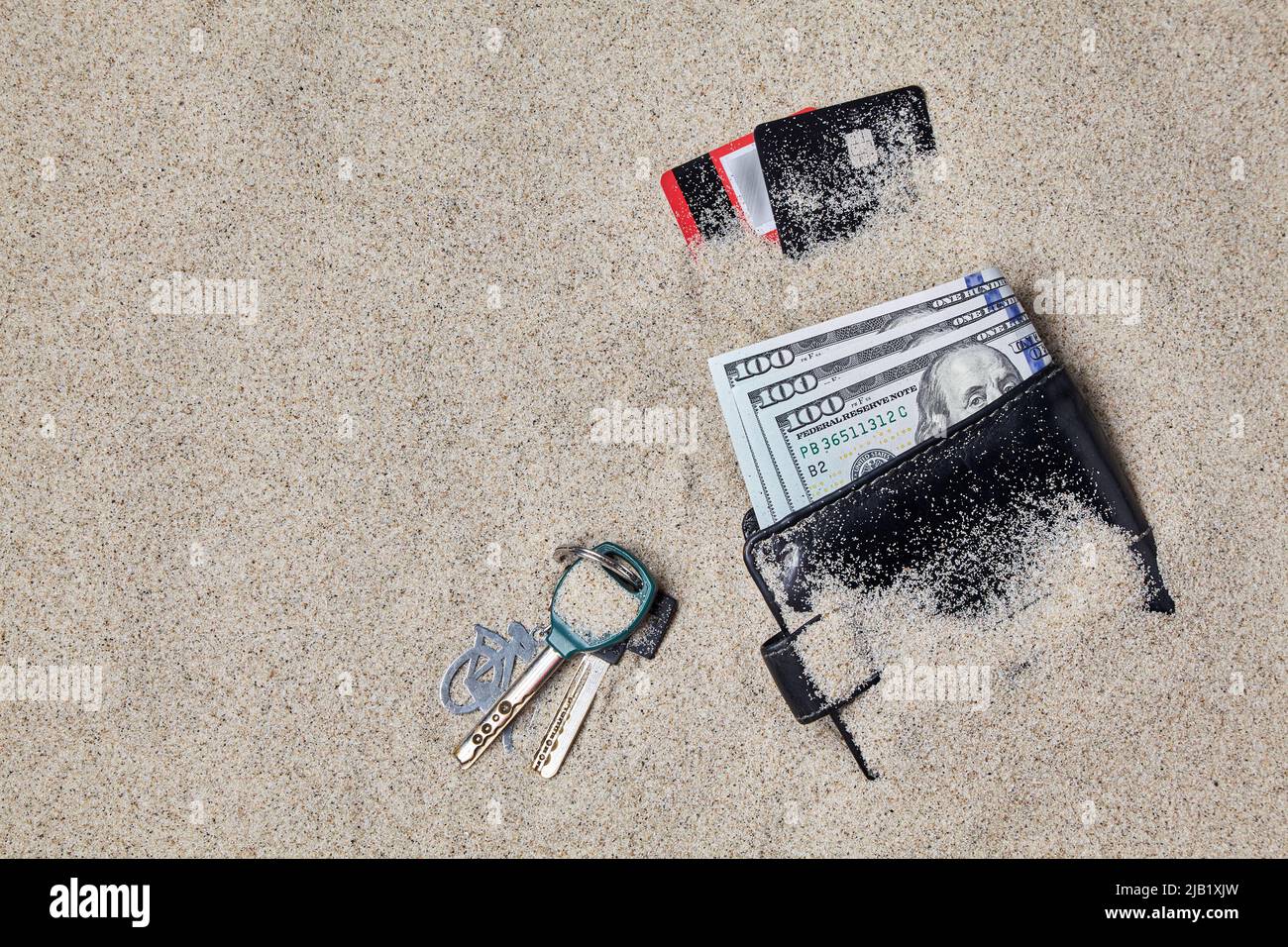 Wallet, dollars, plastic cards and keys left in the sand. Lost items on