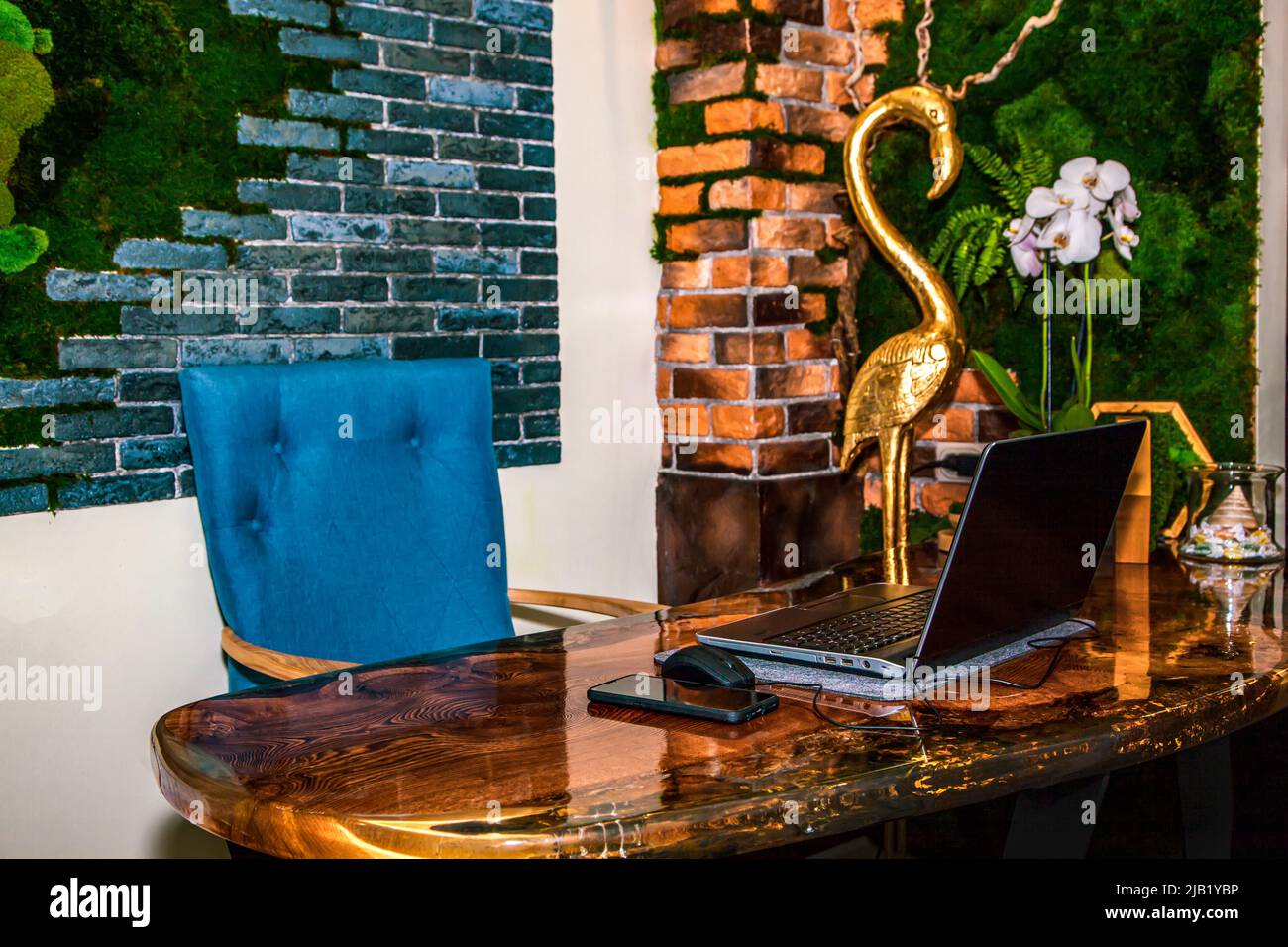 The workplace of an interior designer. Epoxy resin table, brick wall decorated with stabilized moss, laptop, smartphone. Stock Photo