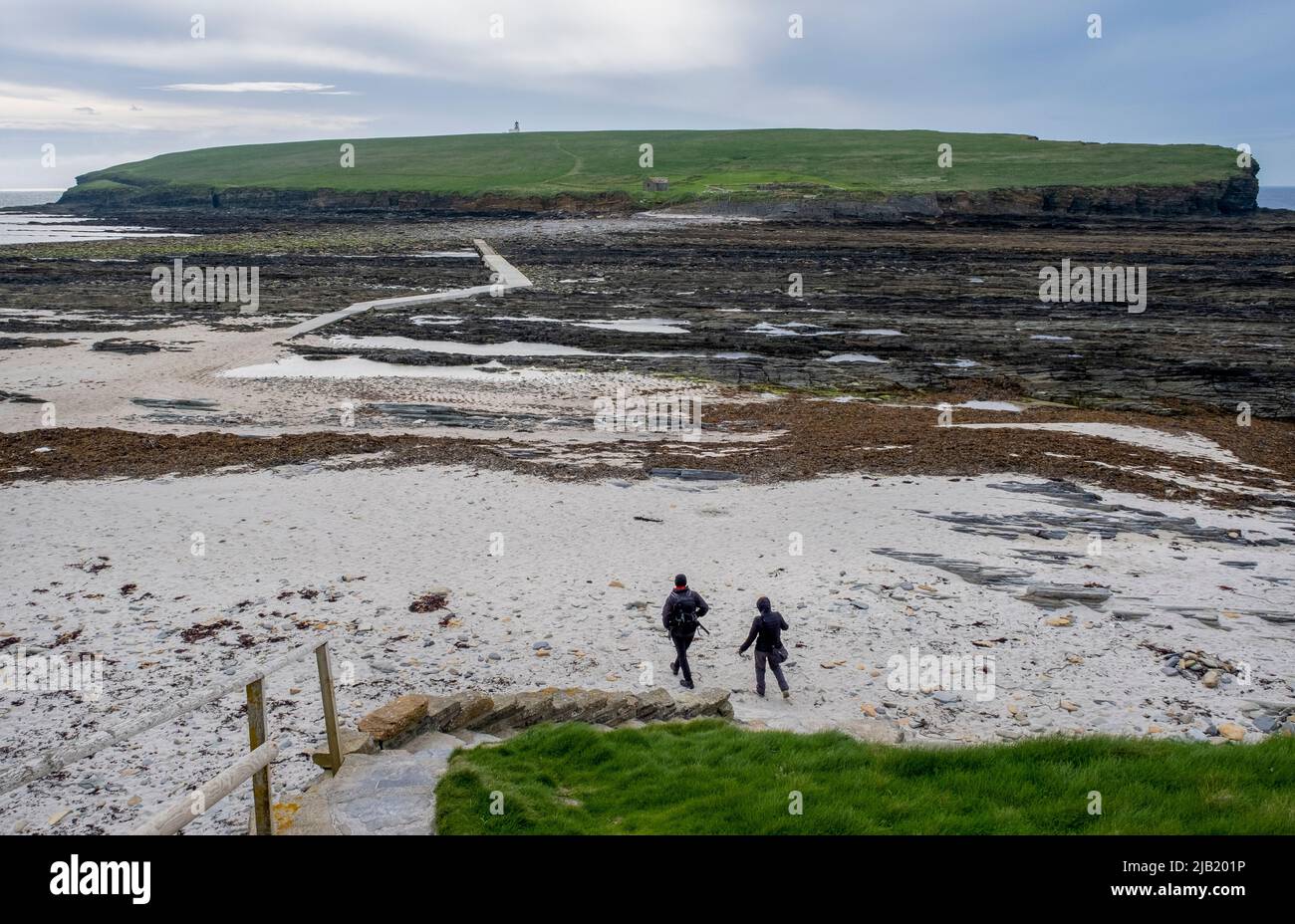 Two people cross from the Orkney mainland at low tide to the Brough of Birsay, Birsay island, Orkney, Scotland. Stock Photo