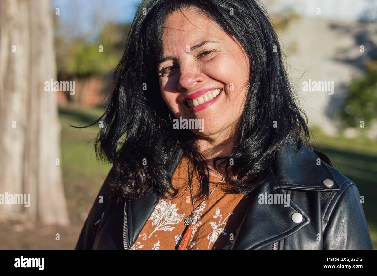 portrait beautiful adult latin woman outdoors as a tourist in a natural park, smiling looking at the camera, on a sunny day. Stock Photo