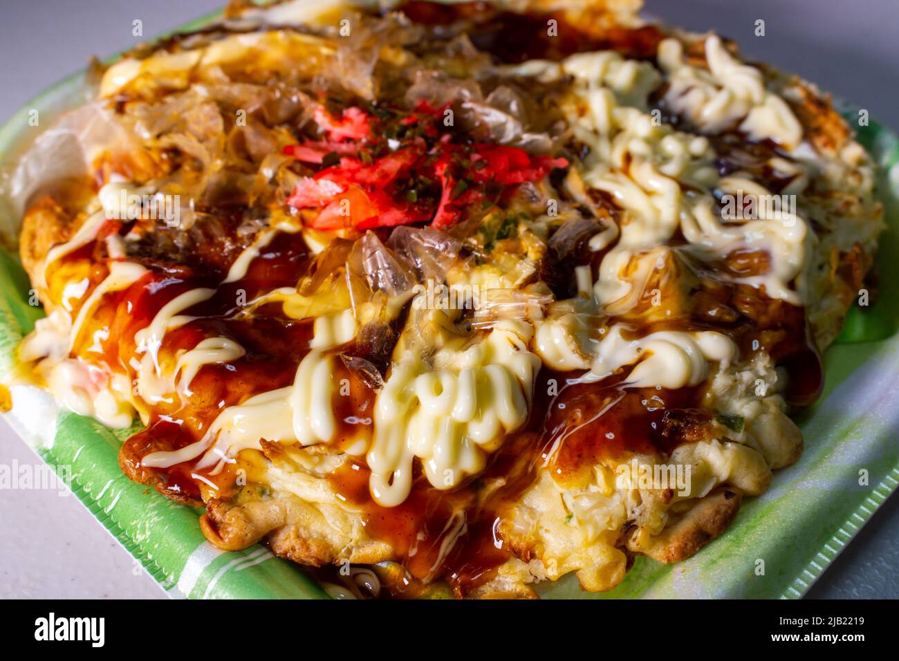 Okonomiyaki, Japanese pancake dish consisting of wheat flour batter & other ingredients, topped with mayonnaise & okonomiyaki sauces in the food tray Stock Photo