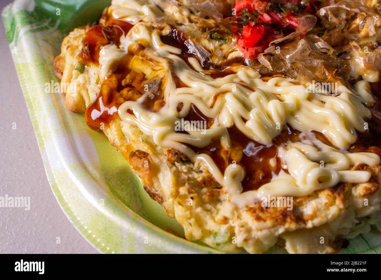 Okonomiyaki, Japanese pancake dish consisting of wheat flour batter & other ingredients, topped with mayonnaise & okonomiyaki sauces in the food tray Stock Photo