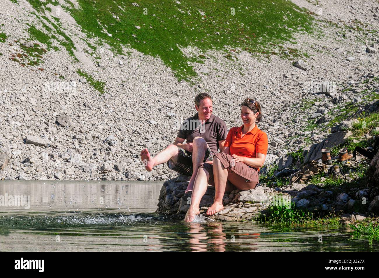 Couple enjoying morning sun while sitting at the Koblatsee near the Nebelhorn in Allgäu Alps Stock Photo