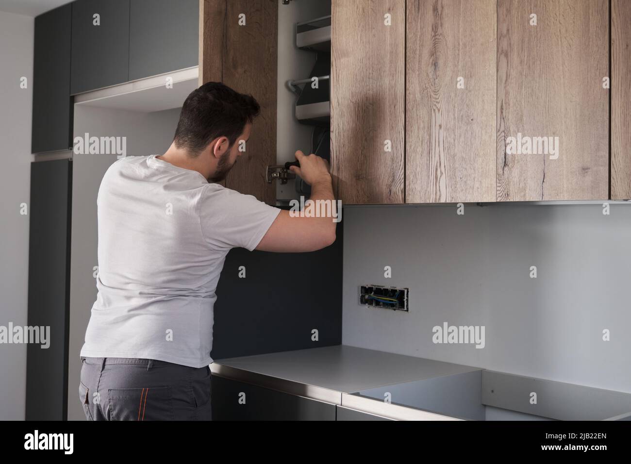 Young argentinian man installing cabinet in the kitchen using a screwdriver. Stock Photo