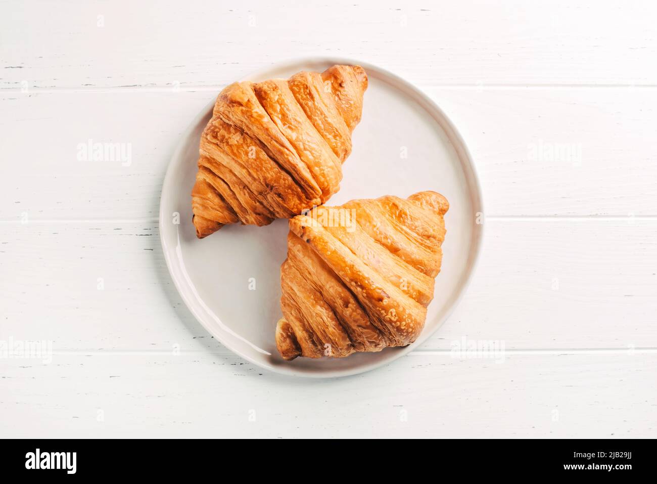 Plate with two fresh croissants on white table. Stock Photo