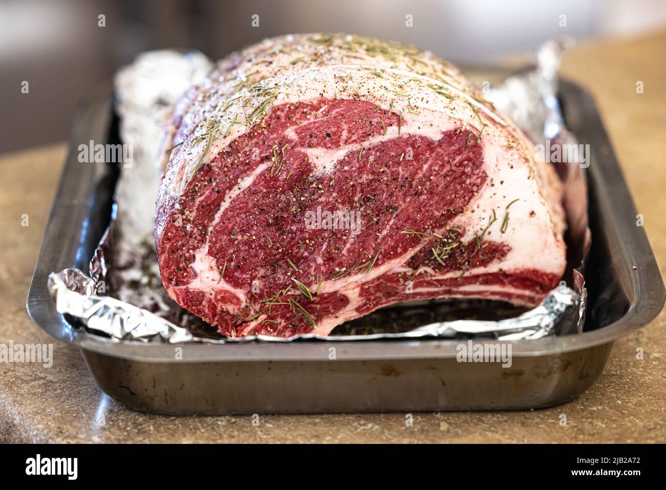 Raw prime rib roast seasoned and sitting on an aluminum foil lined pan ready for the oven for a holiday Christmas dinner Stock Photo