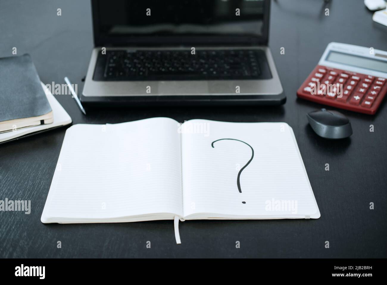 Question mark in a notepad on the background of a laptop and a
