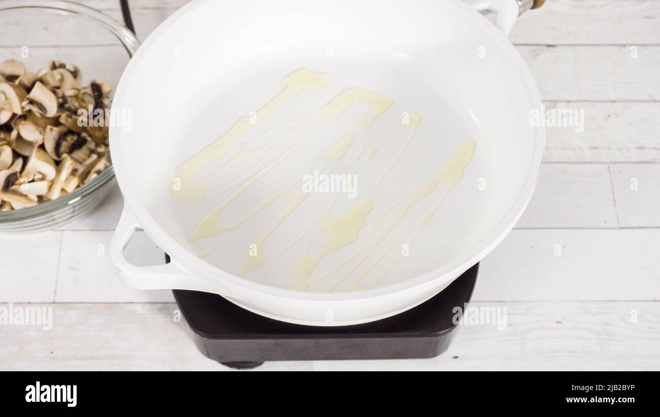 Sauteed organic baby bella mushrooms in a white frying pan Stock Photo