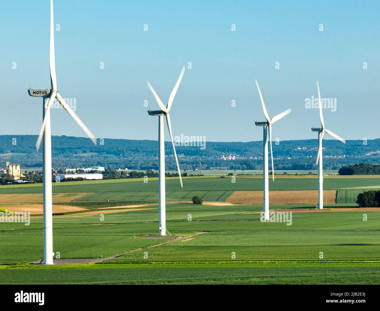 Perspective view of sustainable agriculture fields featuring four wind turbine poles for renewable energy with misty forest in the background Stock Photo