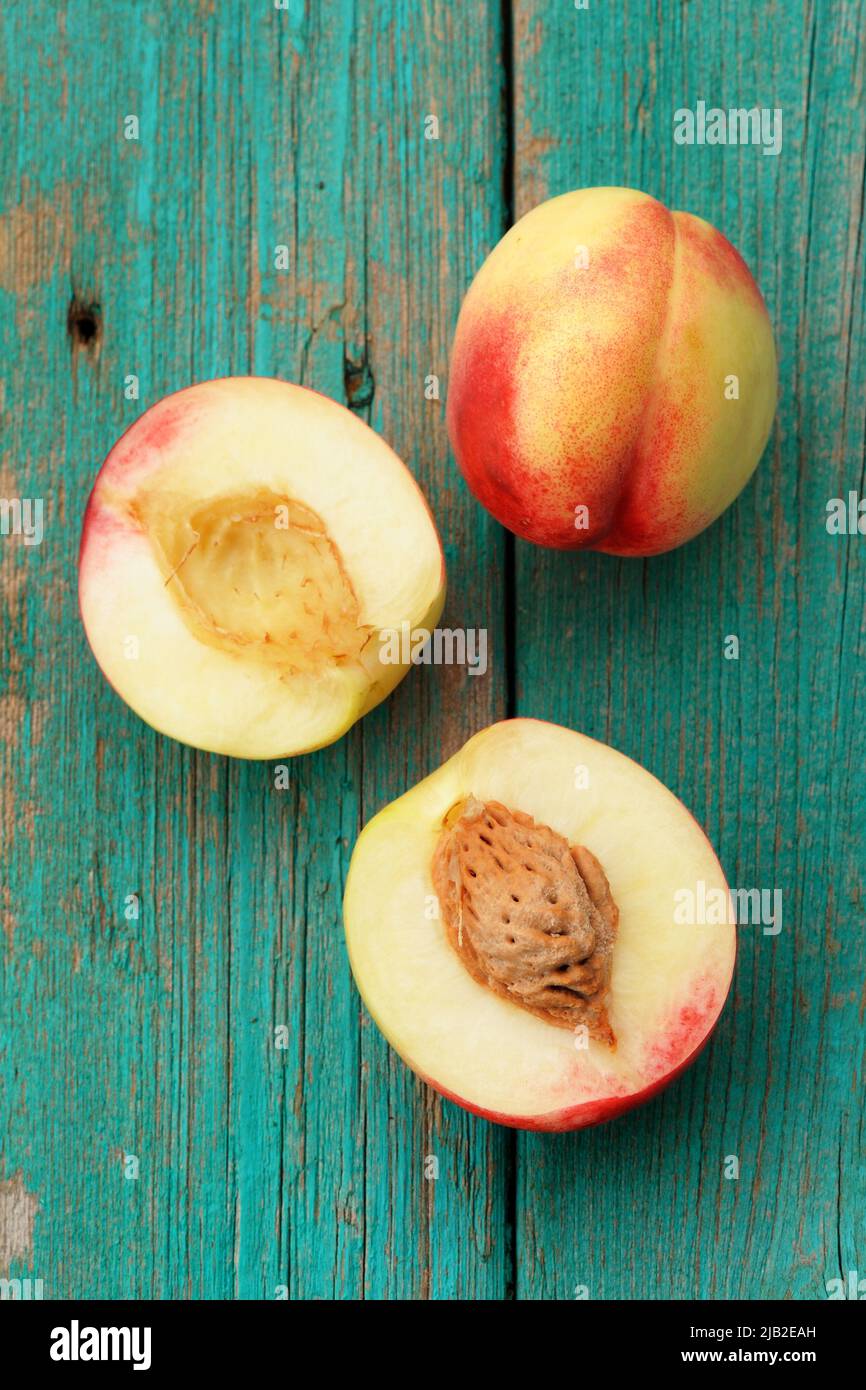 Two nectarines, whole and split on vintage turquoise table vertical Stock Photo