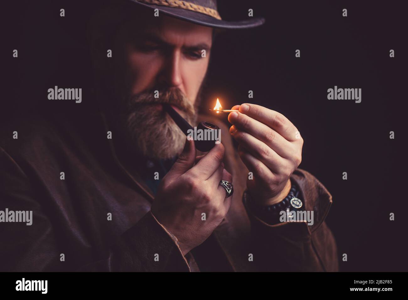 Bearded man wearing hat and smoking a pipe, looking very serious Stock