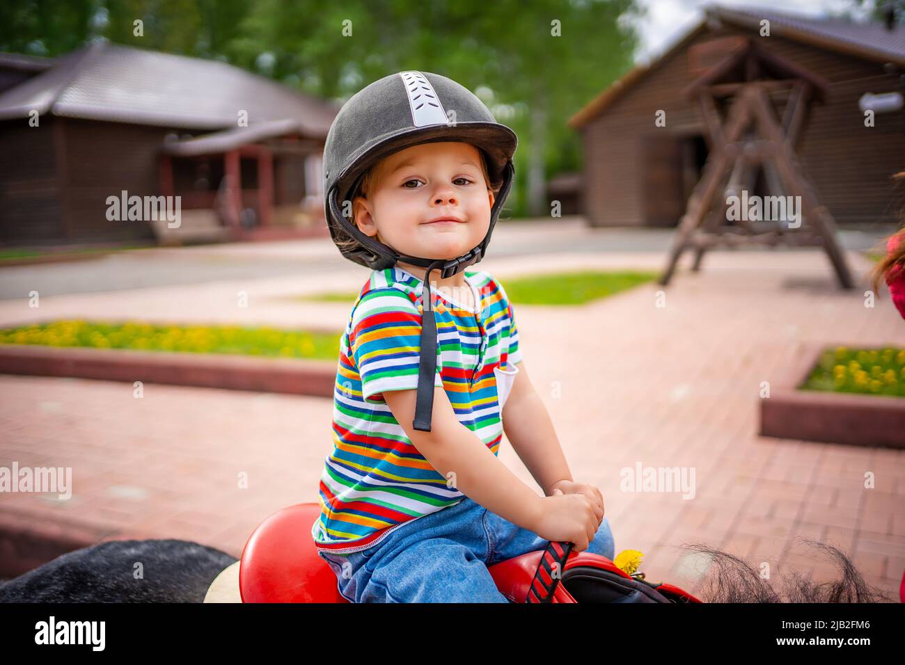 Beautiful little girl two years old riding pony horse in big safety