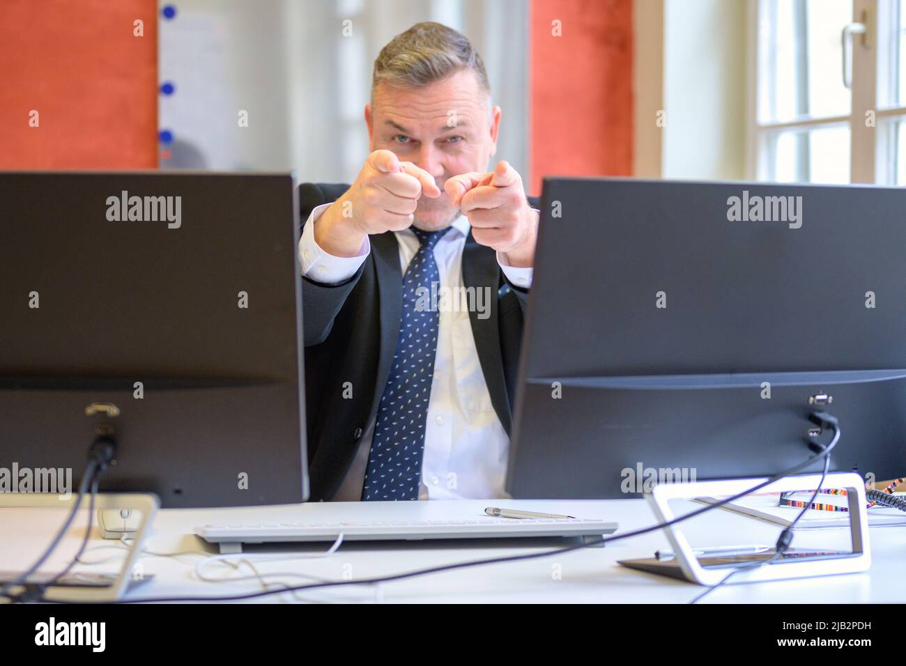 Businessman pointing with both hands at the camera viewed between computer monitors Stock Photo