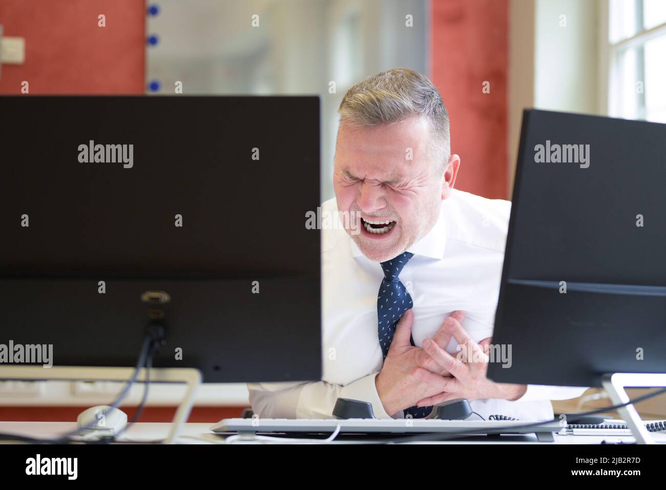 Businessman suffering a heart attack in the office clutching at his