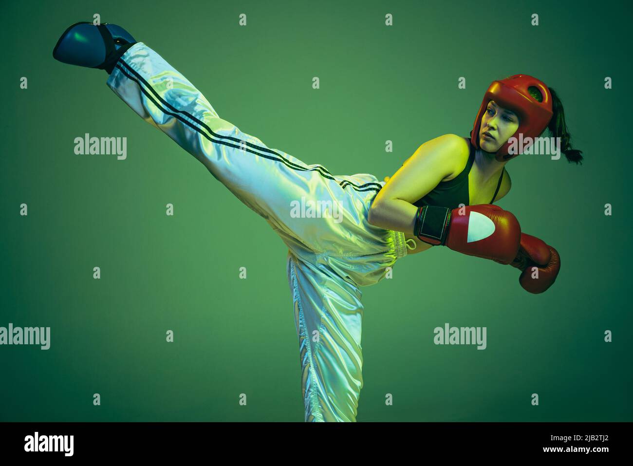 Leg kick. Flexible female boxer in boxing gloves and helmet practicing