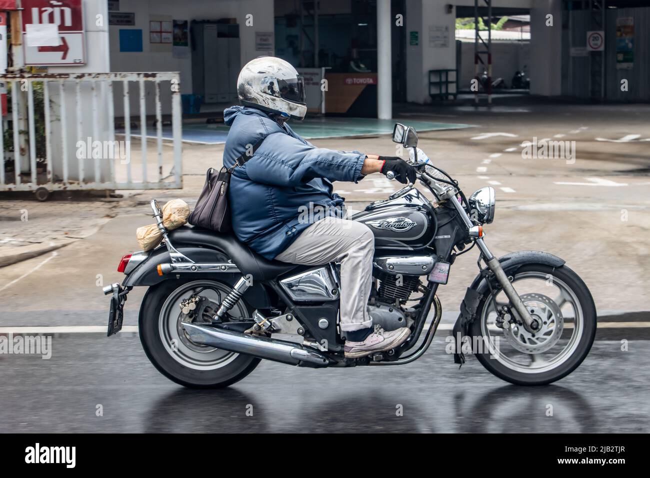 SAMUT PRAKAN, THAILAND, MAY 08 2022,  A man drives a motorcycle on a wet city street Stock Photo