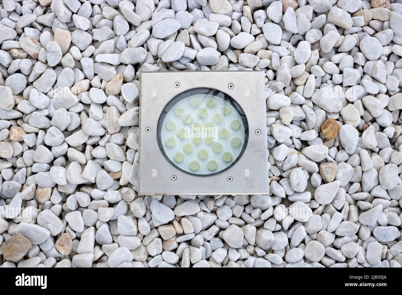 Built-in modern round-shaped lamp on white gravel in the garden. Stock Photo