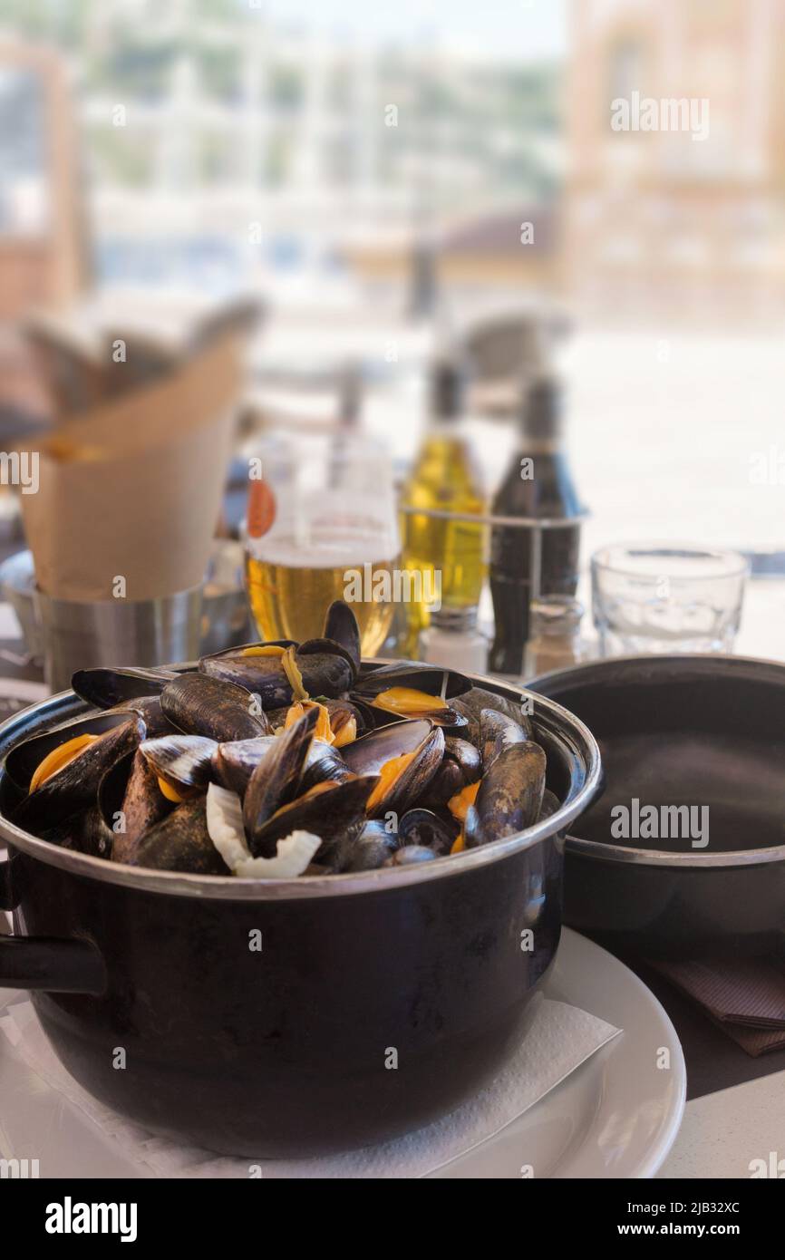 Cooked mussels in garlic sauce in a black saucepan on a table in a fish restaurant. Delicious lunch with seafood and beer. Gastronomic travel. Close-u Stock Photo