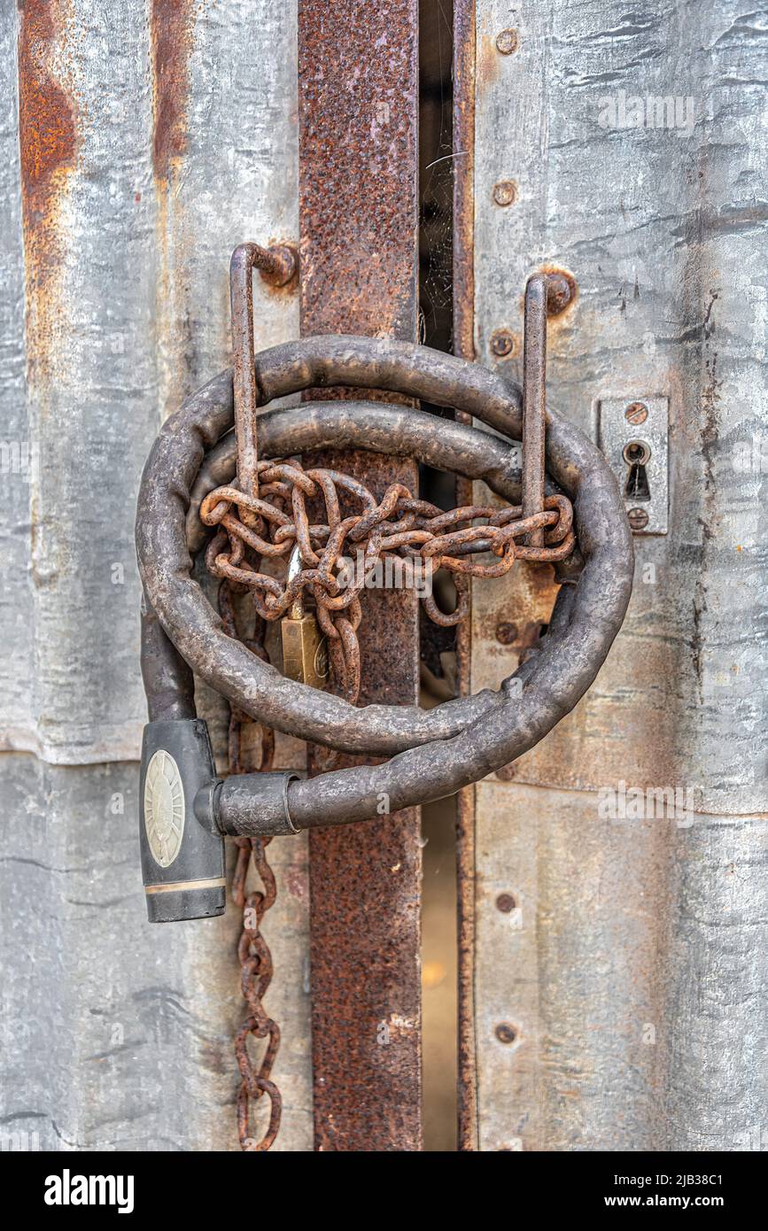 A cluster of rusty locks - old motorbike lock, rusty chain link and padlock, on rusty steel frame doors cladded with rusty corrugates metal sheets. Stock Photo