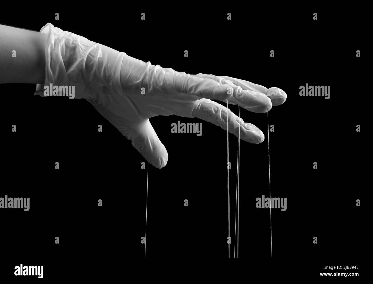 Hand in medical glove with strings on fingers. Fraud, manipulation in medicine, conspiracy theory concept. Black and white. High quality photo Stock Photo