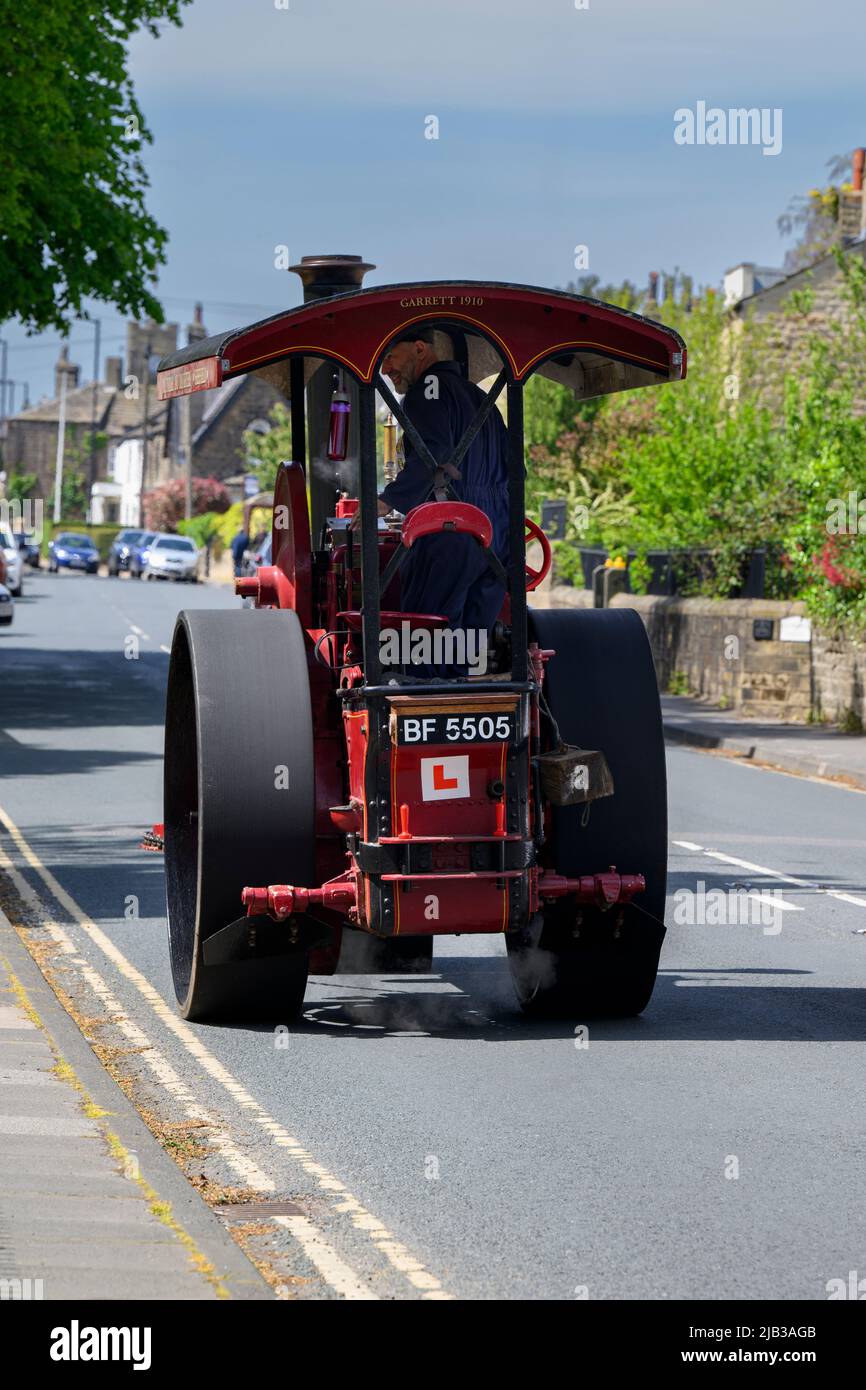 Vintage restored heavy old-fashioned red steam-powered vehicle (black chimney, L-plate, driver) - Burley-in-Wharfedale, West Yorkshire, England, UK. Stock Photo