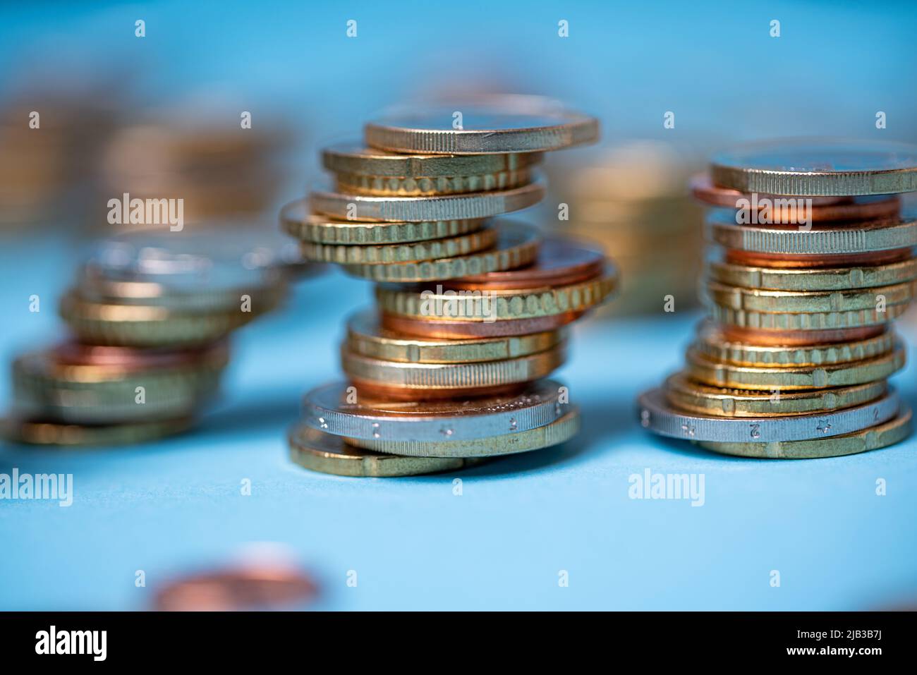 Piled up coins on blue backdrop. Euro coins from European Union. Currency and cash piled up to towers Stock Photo