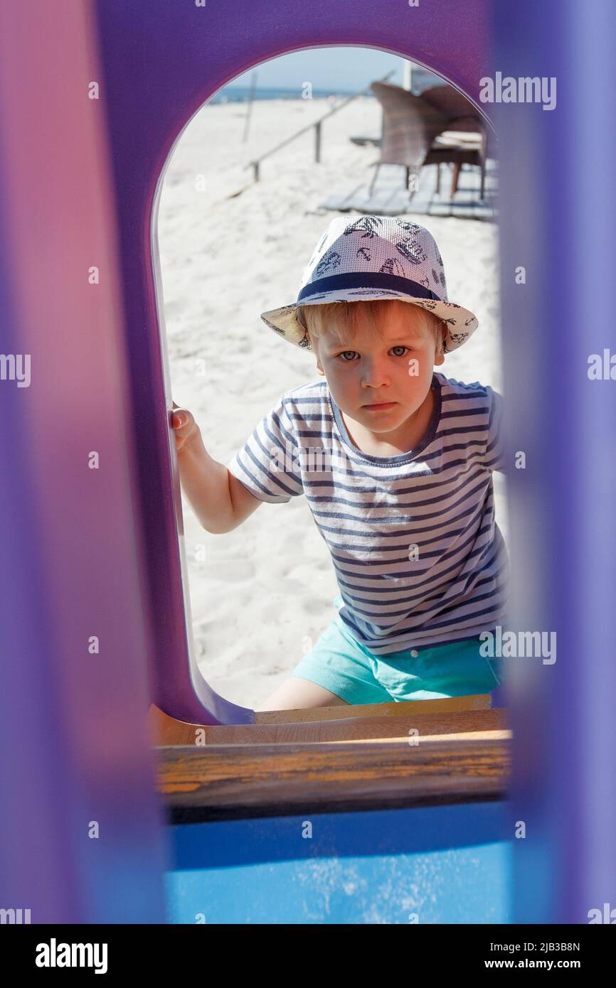 A portrait of a boy in the background of a beach playground. Framing a purple plastic arch Stock Photo
