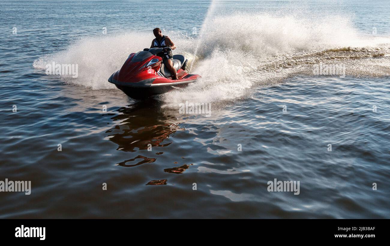 Man drives red jet ski on turquoise sea on a blue day Stock Photo