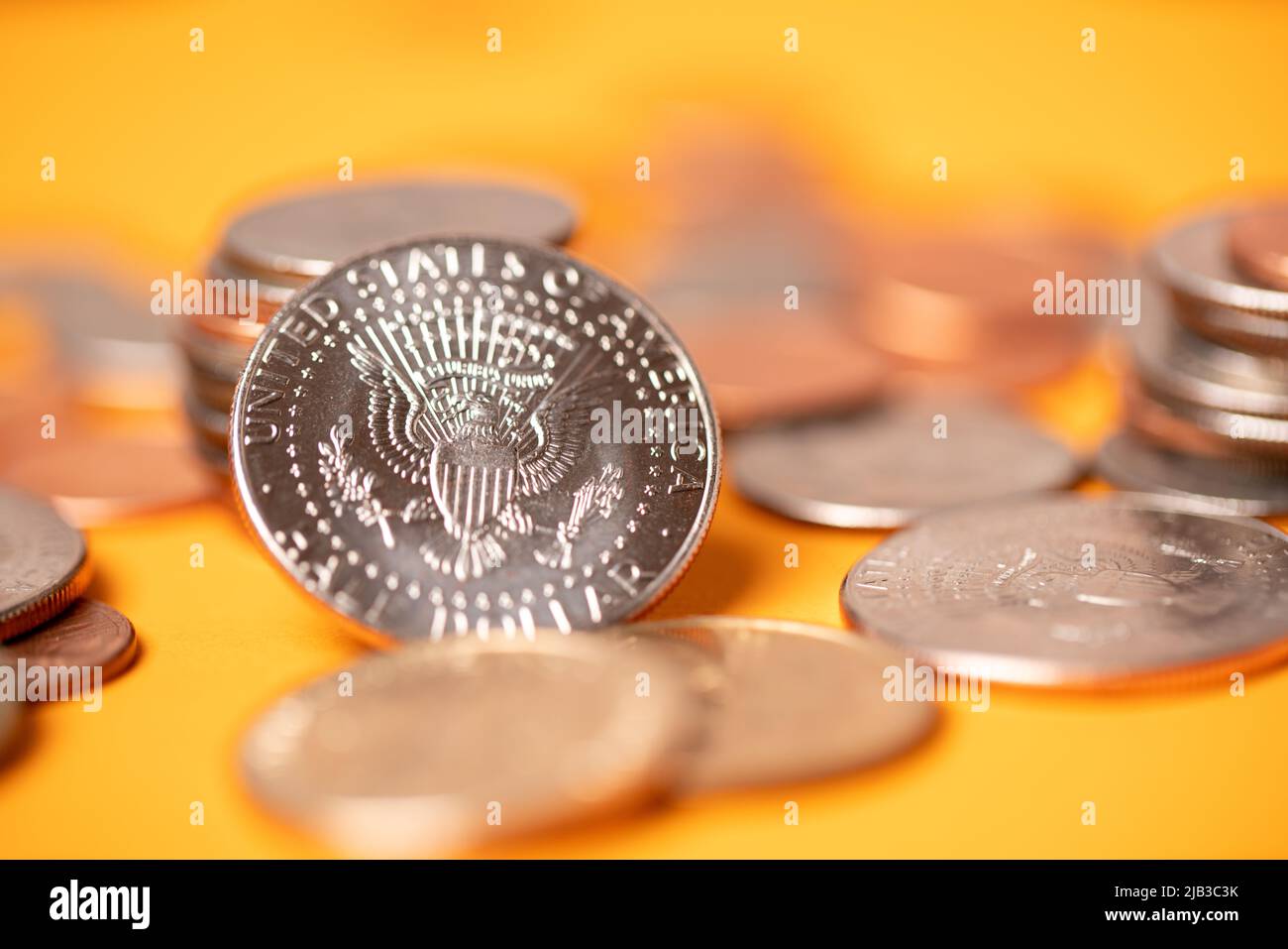 US dollar coins on orange background. Half dollar coins piled up with pennies and quarters. Dollar currency stacked and piled up Stock Photo