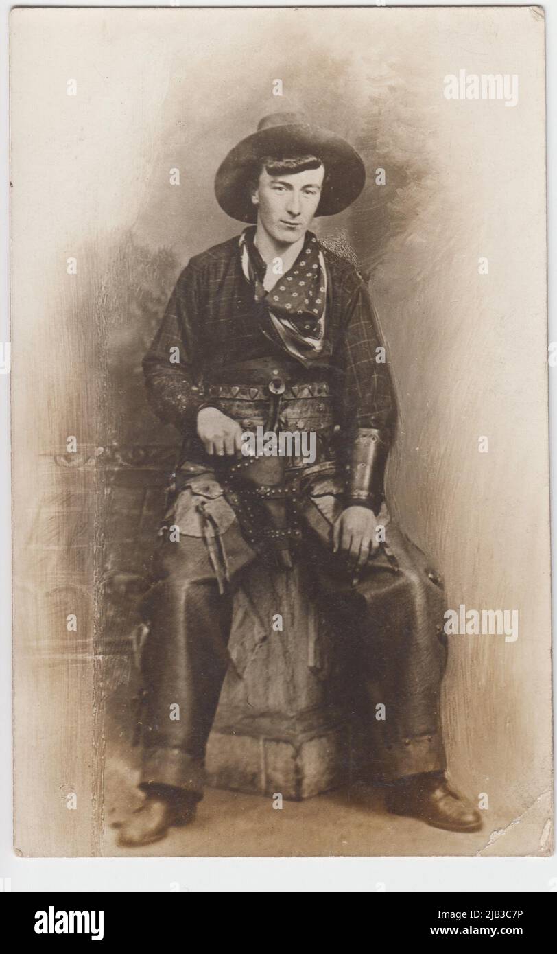 Studio portrait of a cowboy, with cowboy hat, US flag bandana, checked shirt, gun in holster & leather trousers. It may show a performer in one of the Wild West shows which toured the UK in the early 20th century Stock Photo