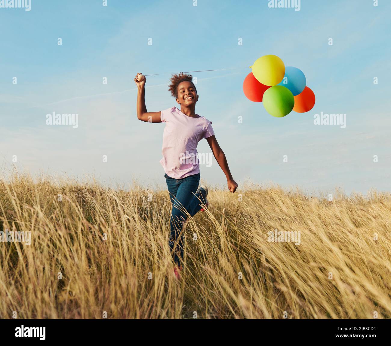Happy little girl running playing with balloons outdoors Stock Photo