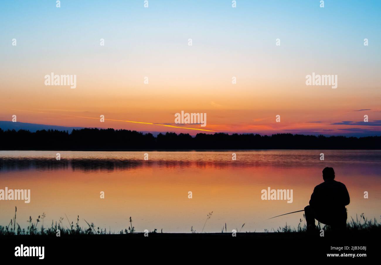 Silhouette of a fisherman with a fishing rod in the morning on a fishing trip. Peaceful sunrise on the lake Stock Photo