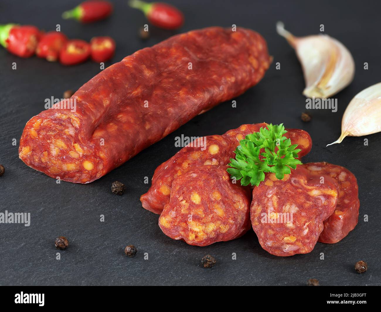 Spanish traditional chorizo sausage with fresh herbs, garlic, pepper and chili peppers served on black slate board, close up. Stock Photo