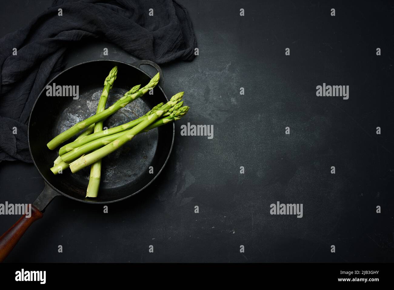 fresh green asparagus in a round cast iron pan on a black table, top view Stock Photo