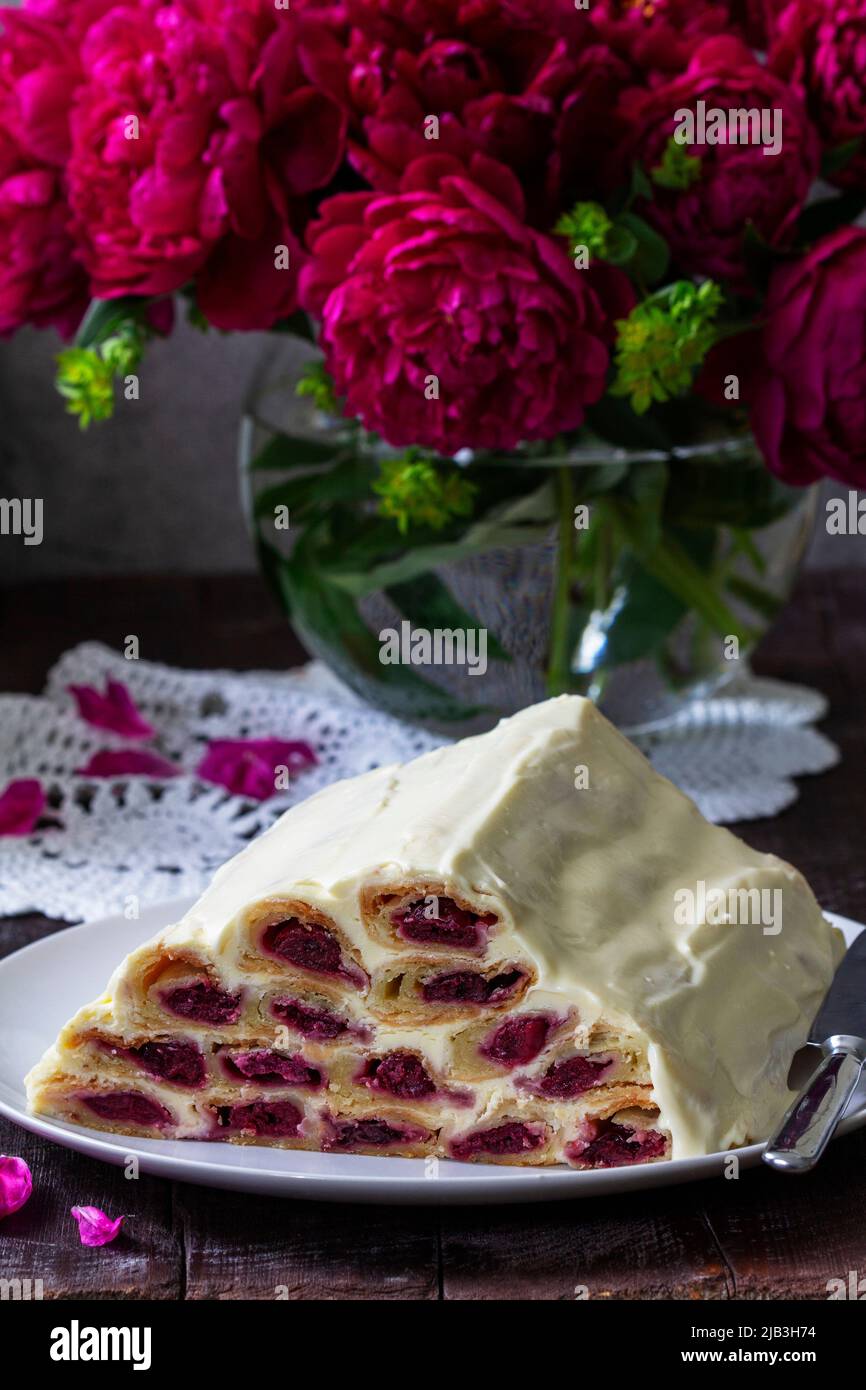 Cake Monastic hut with cherry filling and sour cream, a bouquet of peonies on a wooden table. Stock Photo