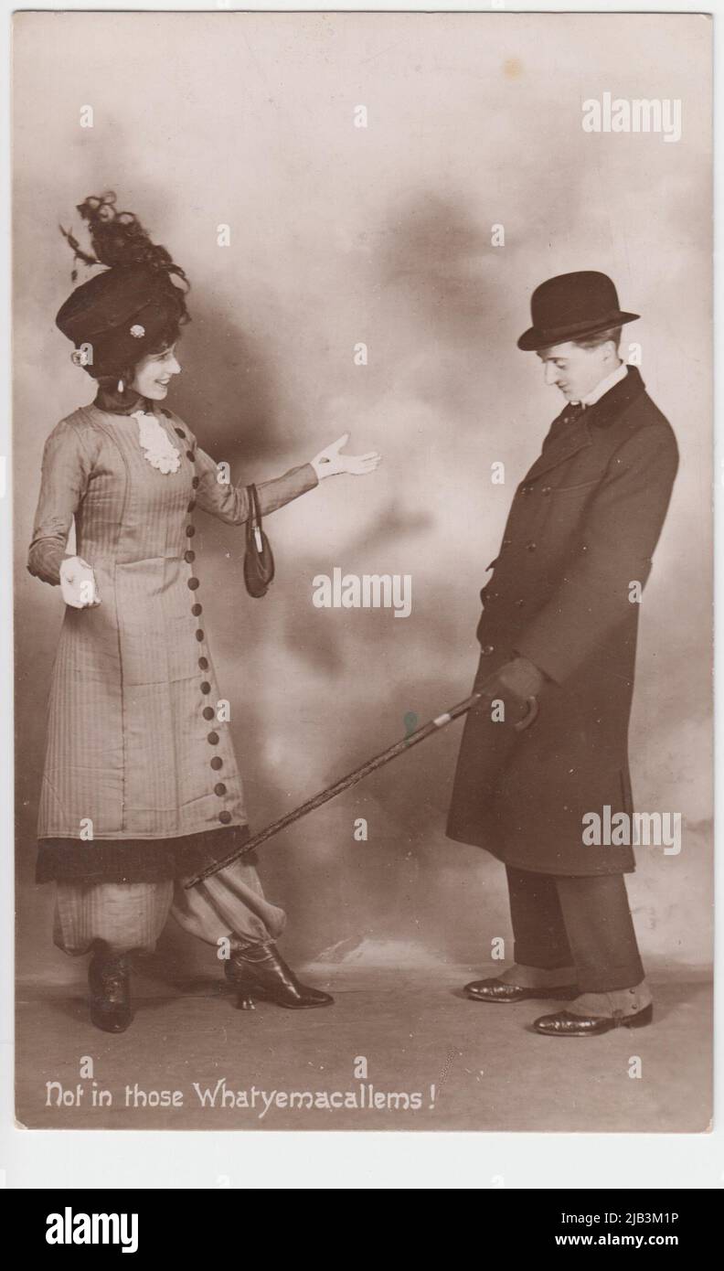 'Not in those Whatyemacallems!': a take on 'Not in those trousers', a phrase popularly associated with women in bloomers or harem pants in the early 20th century. The comic photograph shows a man in suit, overcoat and bowler hat pointing his umbrella at a woman's legs. She is standing dressed in fine clothes, including a feathered hat, coat and trousers Stock Photo