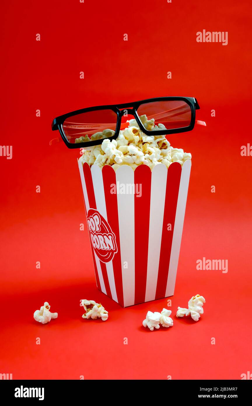 Fresh popcorn in a striped paper cup with 3d glasses on a red ...