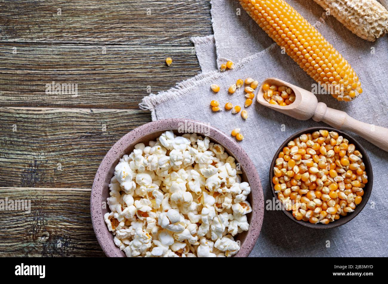 Corn kernels, cob, freshly popped popcorn on wooden background with