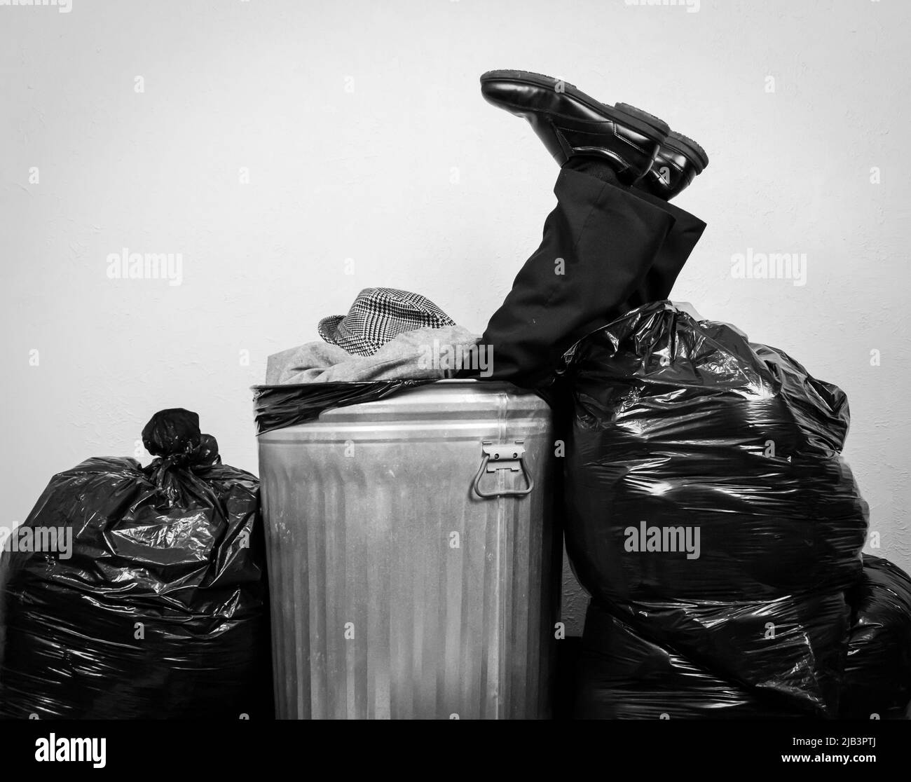 Businessman in Suit Sitting in Rubbish Bin Surrounded by Garbage Bags. Concept of Being Thrown Away by Capitalism and Greed. Stock Photo