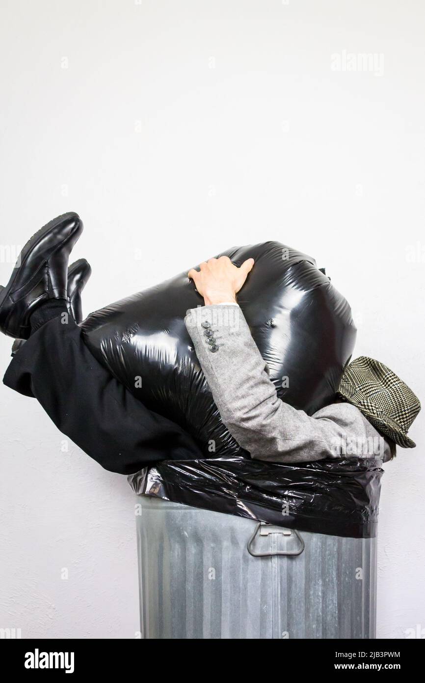 Businessman in Suit and Hat Sitting in Metal Trash Can With Garbage Bag on Top of Him. Concept of Crushed by Rubbish. Stock Photo