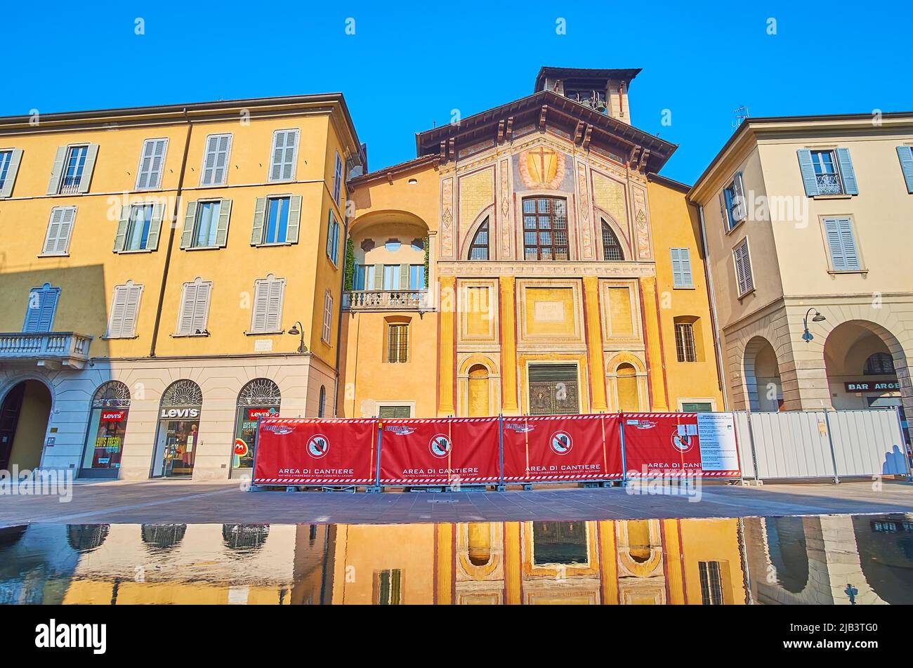 The ornate frescoed medieval San Giacomo Church, located on Piazza Guido Grimoldi with a giant puddle, reflecting the yellow church facade, Como, Lomb Stock Photo